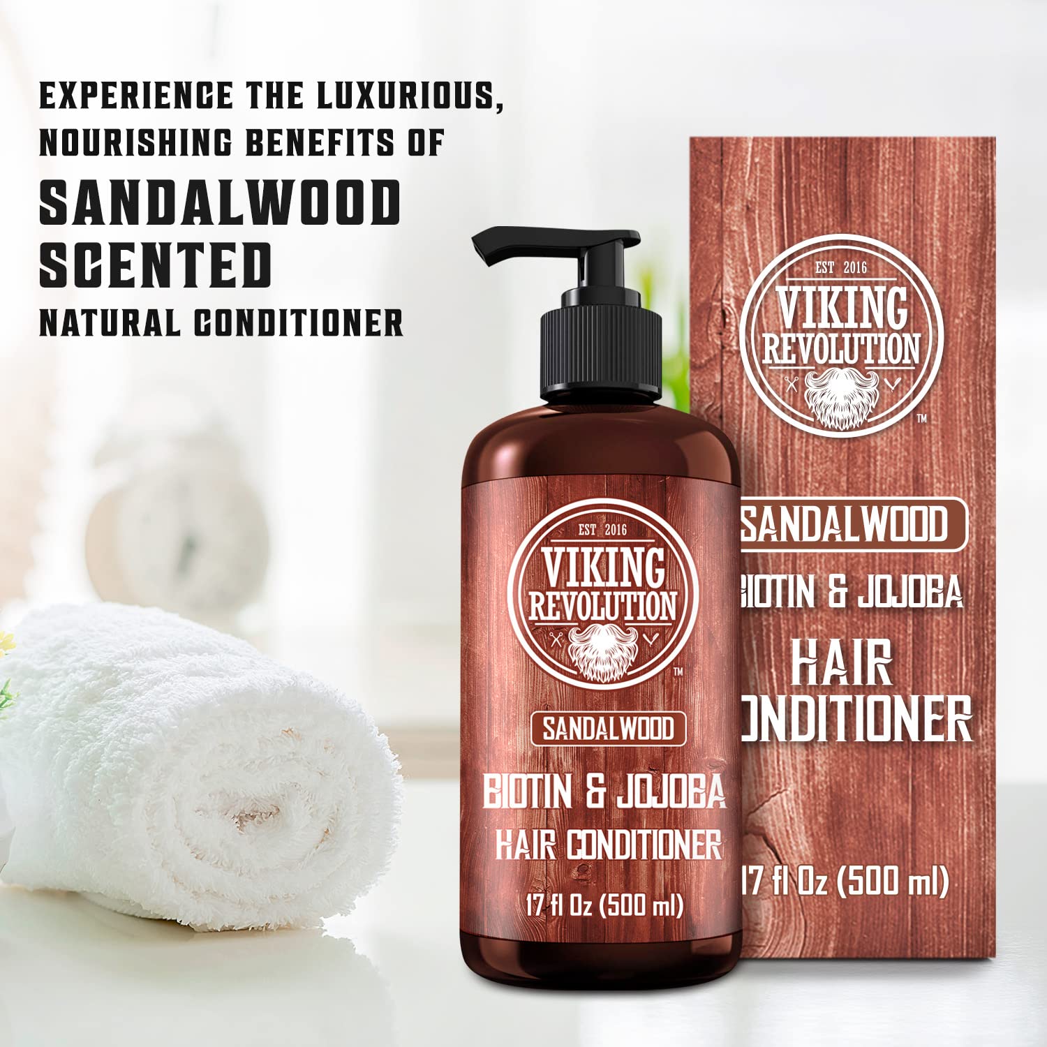 A bottle of Sandalwood Conditioner with Biotin and Jojoba Oil (17 Oz) is elegantly positioned next to a box and towel on the bathroom counter.
