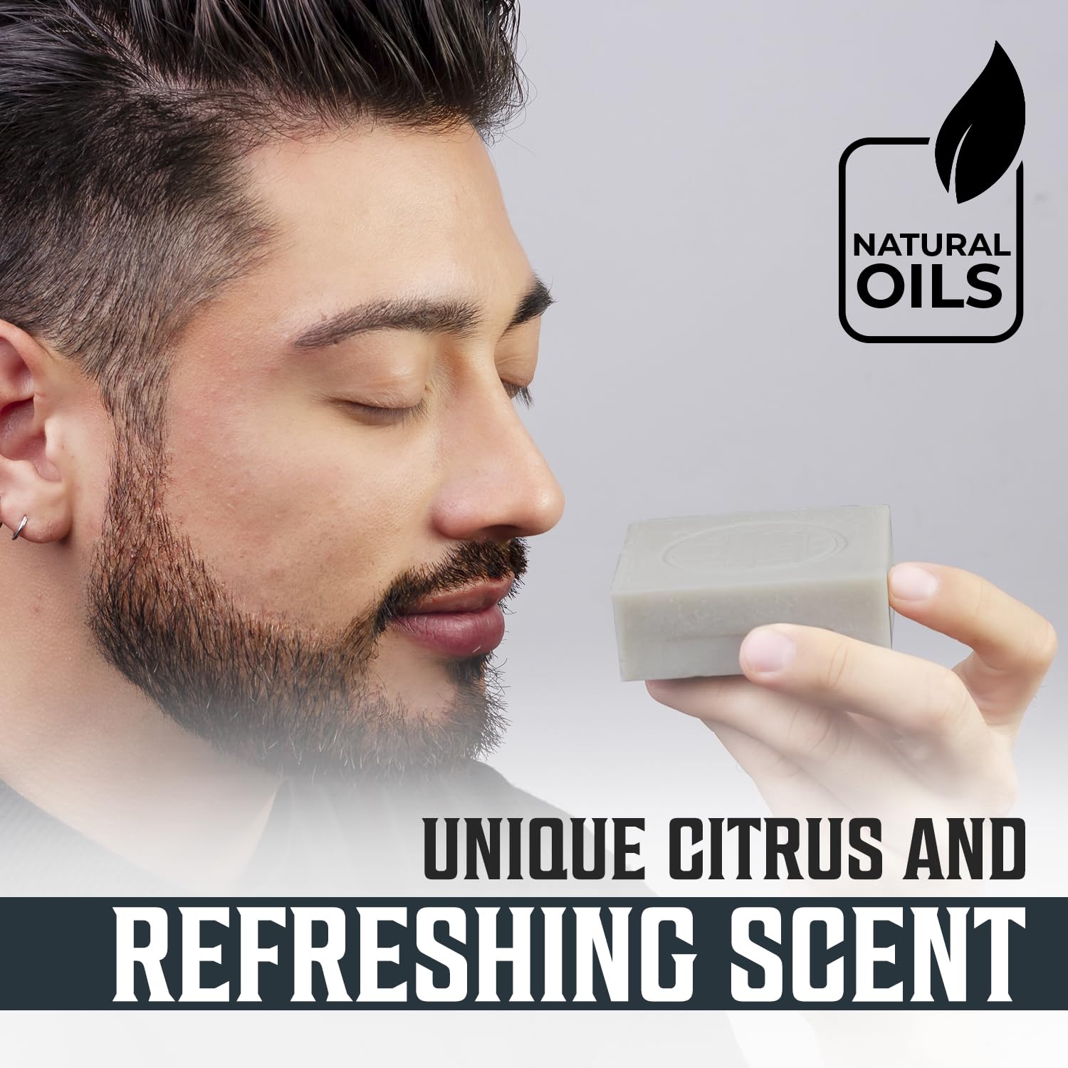 A man holds and sniffs a gray bar of Peppermint Natural Soap for Men, appreciating its refreshing invigorating blend of citrus scents. The soap, embossed with the Natural Oils logo, offers a sulfate and paraben-free formulation with hints of peppermint that add an extra layer of revitalizing freshness.