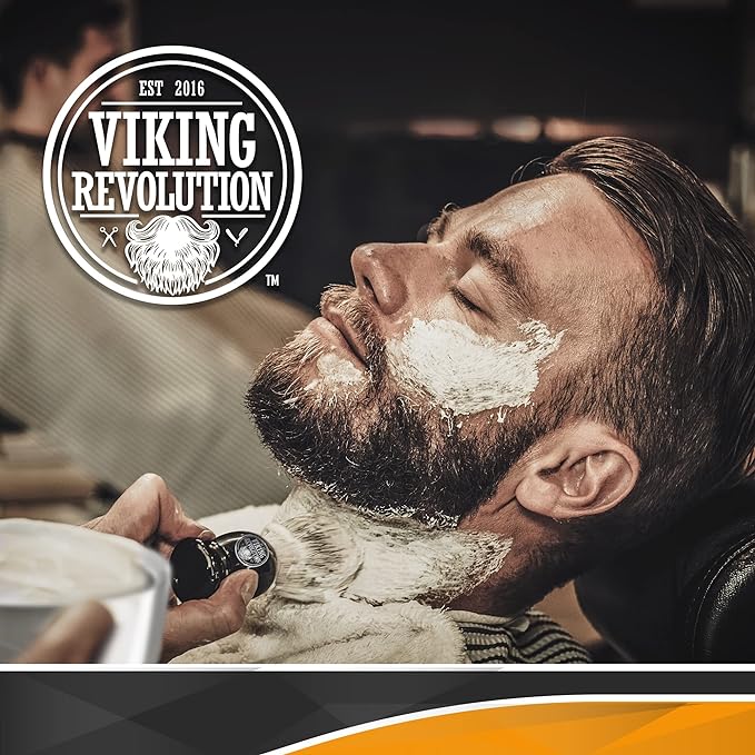 A man sits in a barber chair, enjoying a wet shave with rich shaving cream applied using the Badger Hair Shaving Brush, as the Viking Revolution logo proudly shines above him.