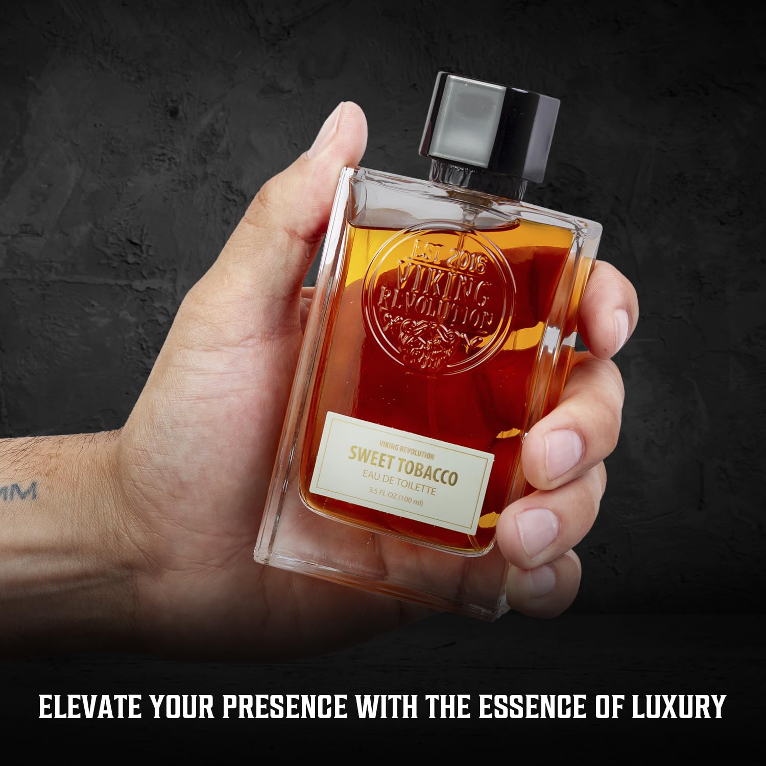 A hand holds a bottle of Cologne for Men 3.5 fl oz against a dark background, capturing the essence of Viking Revolution. This men's fragrance with subtle sandalwood notes exudes an aura of timeless elegance.