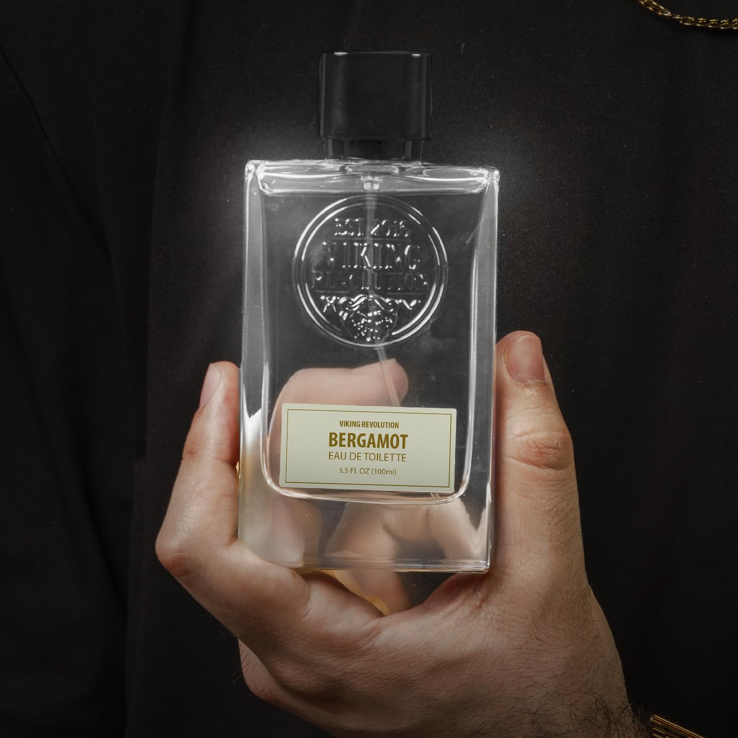 A person holds a clear bottle of Cologne for Men 3.5 fl oz, an exquisite fragrance that captures the essence of adventure.