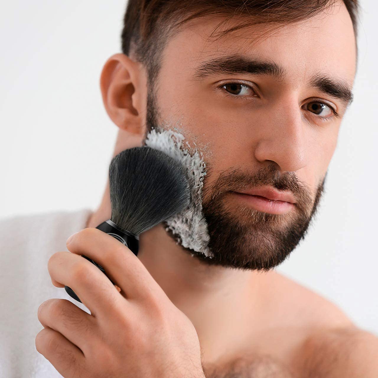 A man expertly applying shaving cream with a Badger Hair Shaving Brush on his beard, wearing a towel around his shoulders for the perfect wet shave.