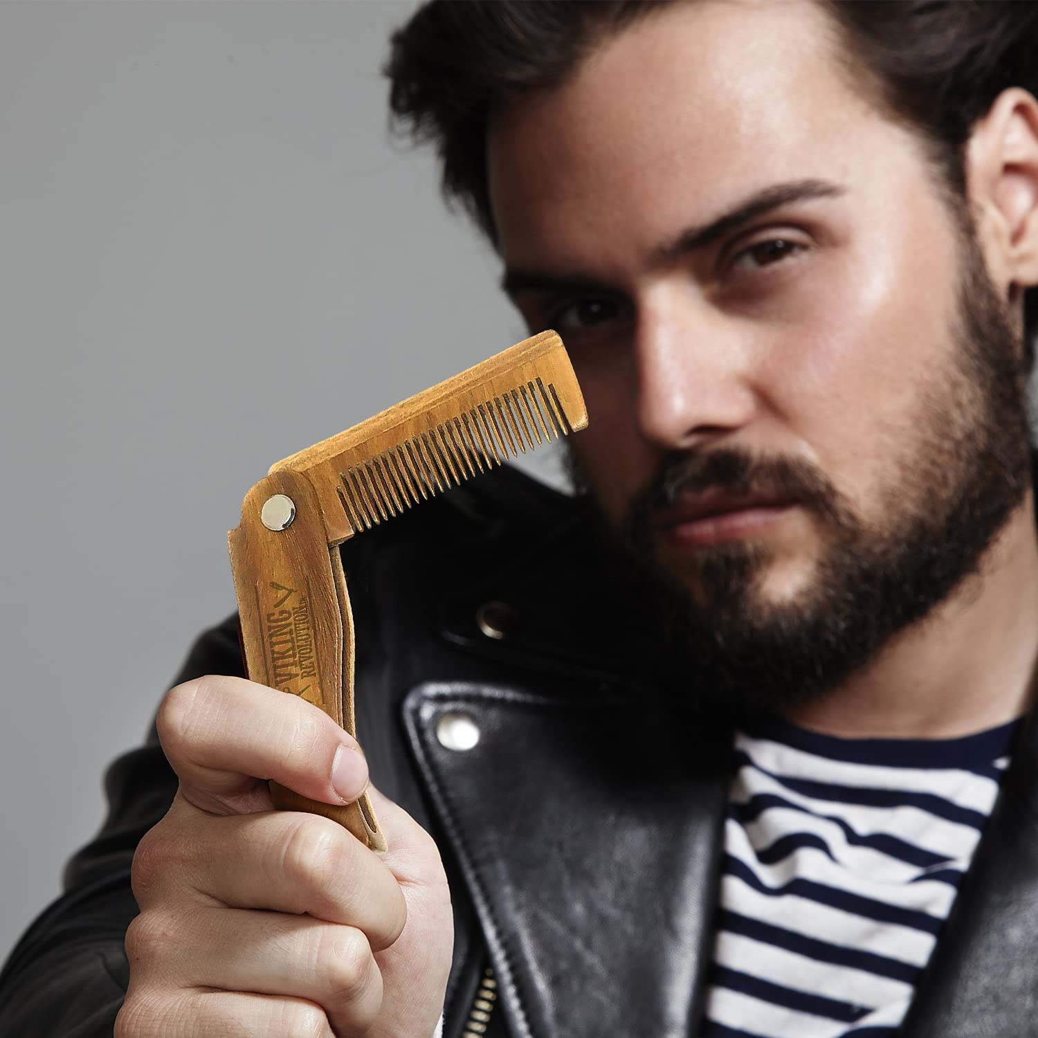 A man confidently holds a Folding Beard Comb with Carrying Pouch, perfectly pairing it with his leather jacket and striped shirt for the ultimate beard grooming accessory.