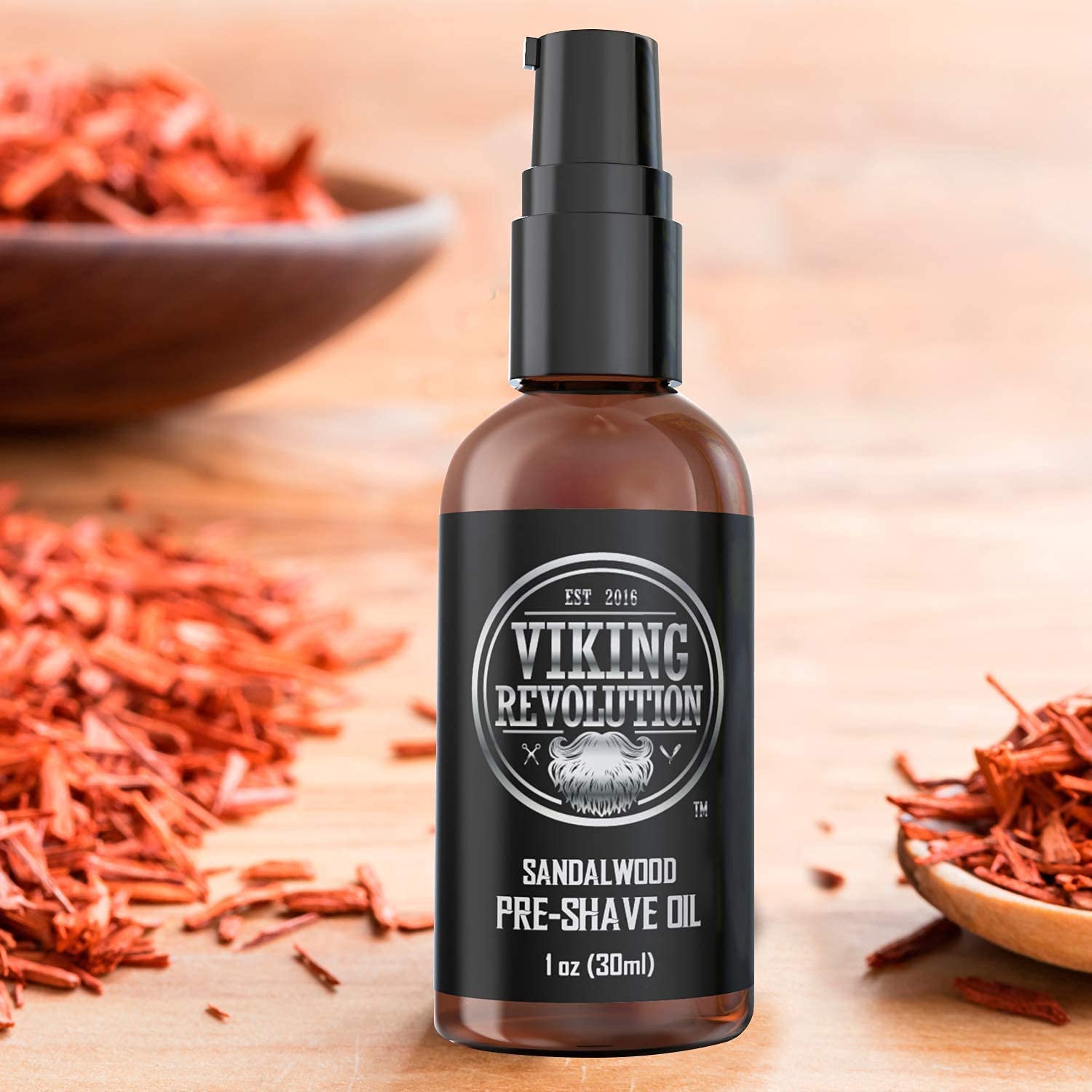 The bottle of Sandalwood Pre-Shave Oil rests on a wooden surface in the midst of sandalwood pieces, offering a smooth, clean shave with its luxurious sandalwood fragrance.