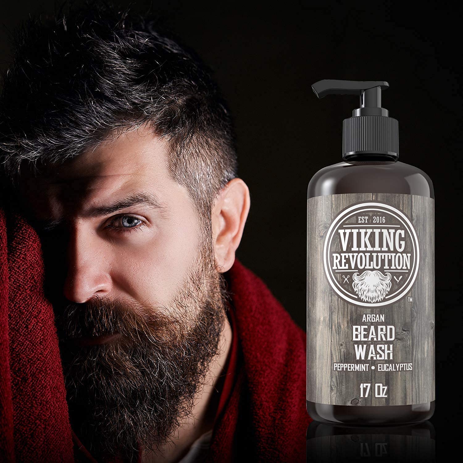 A man with a dark beard stands next to a bottle of Peppermint & Eucalyptus Beard Wash 17oz, ideal for enhancing facial hair growth.