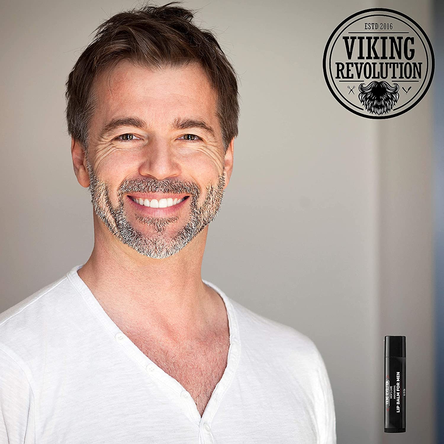 A smiling man with a beard in a white shirt stands next to the Viking Revolution logo and their All Natural Lip Balm for Men - 4 Pack, enriched with Vitamin E.