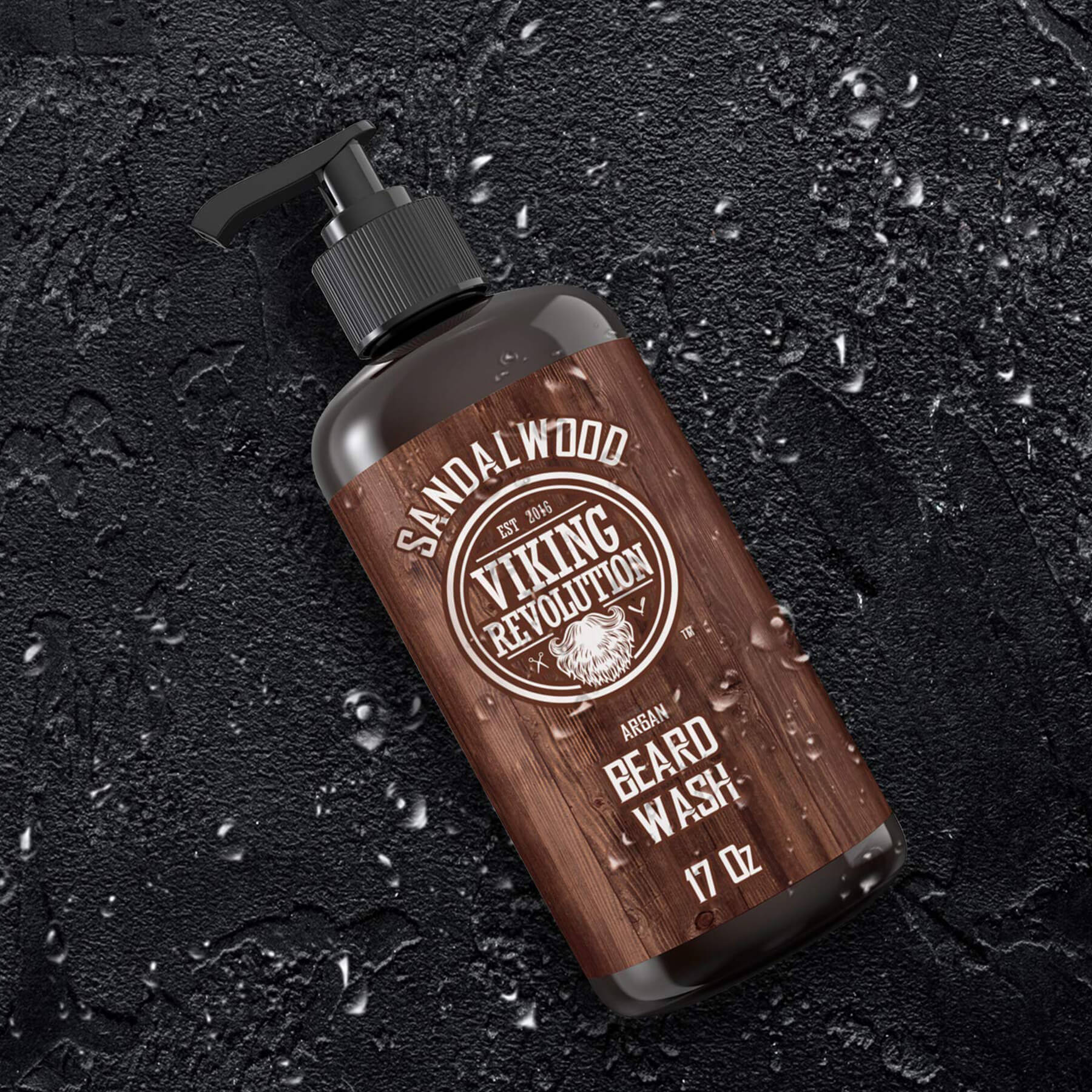 The Sandalwood Beard Wash 17oz bottle from Viking Revolution, celebrated for its sandalwood aroma, sits gracefully on a damp, textured black surface. It promises exceptional beard cleaning with a satisfaction guarantee that assures confidence in every purchase.