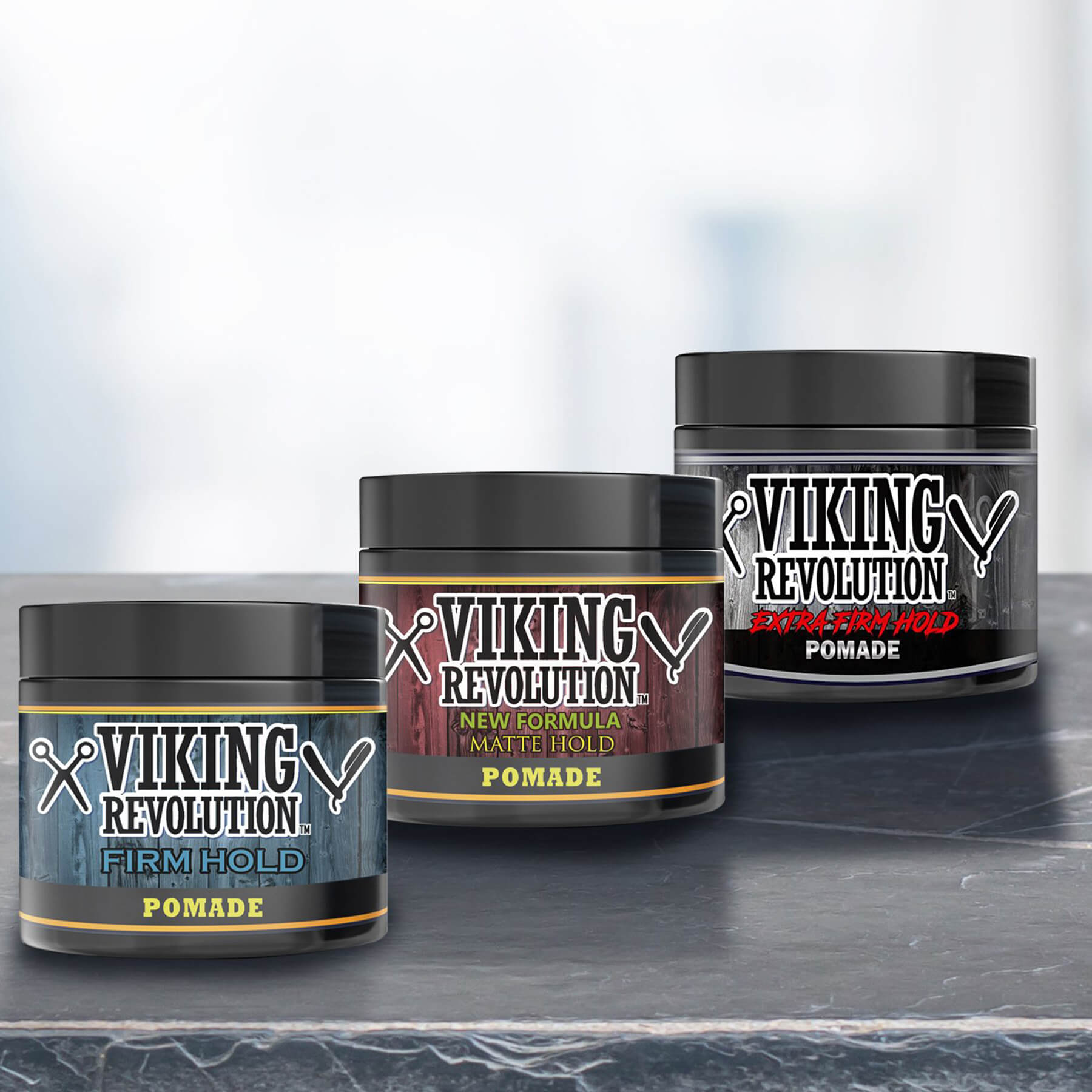 On a dark surface are three jars from the Hair Pomade Mix - 3 Pack, each labeled with varying hold strengths, ideal for creating any hairstyle.