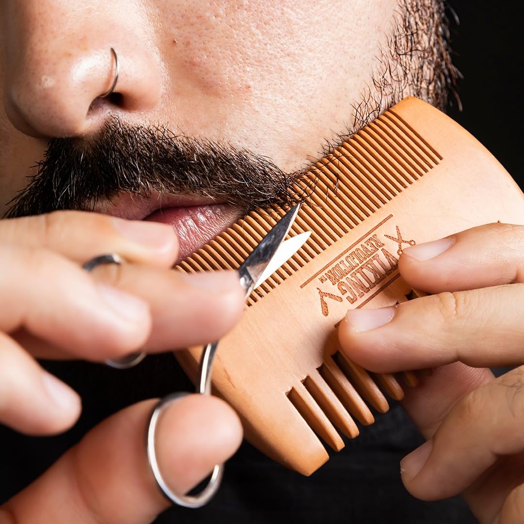 Person trims mustache with scissors and Beard Kit Spiced Vanilla comb.
