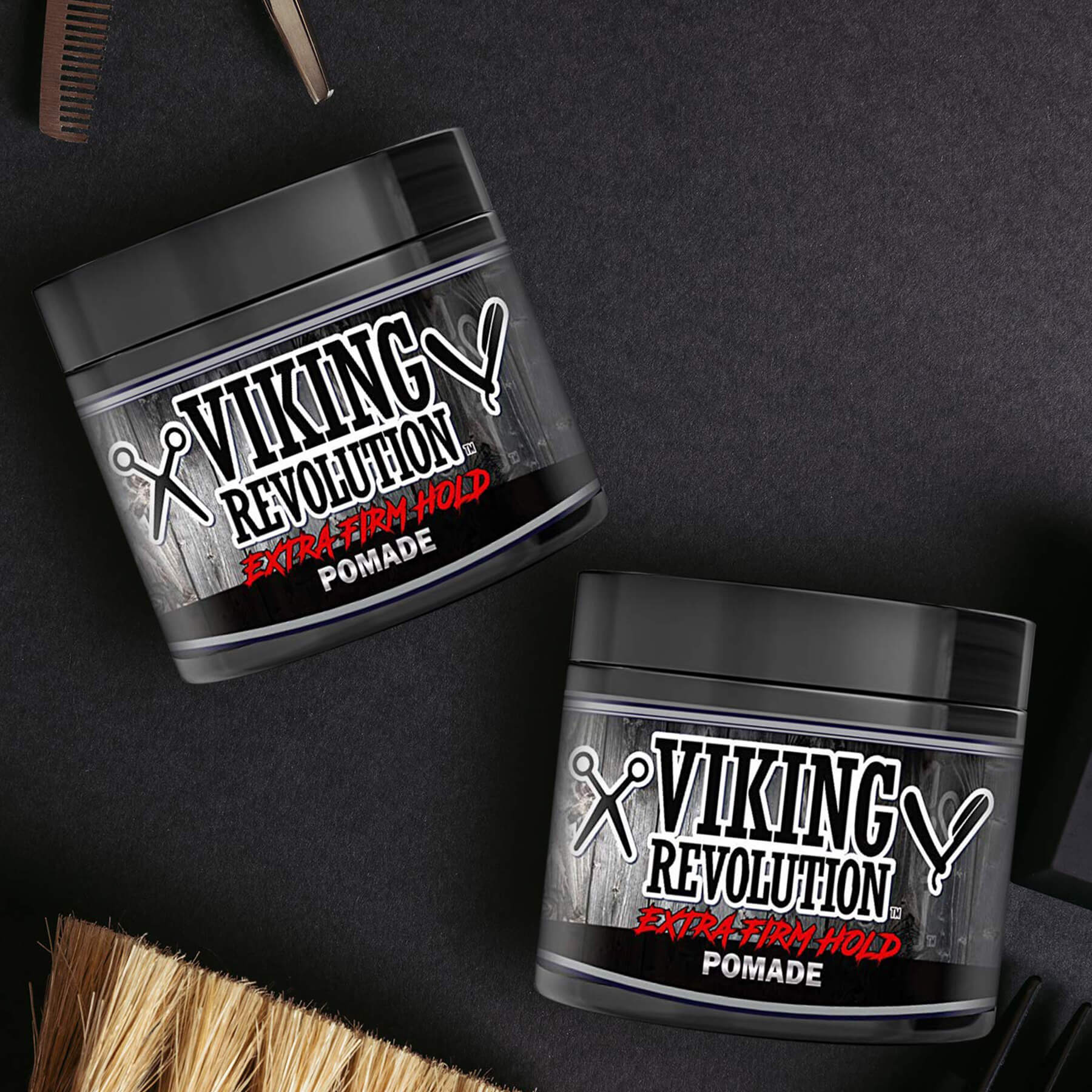 Two Extreme Hold Hair Pomade jars on a black surface with grooming tools for a shiny look.